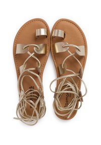 Tan leather sandals with gold metallic straps and crisscross lace design. Features flat soles and loop hardware for adjustable fit.