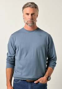 Koszula z długim rękawem i okrągłym dekoltem, wykonana z miękkiego, jasnoniebieskiego materiału. Charakteryzuje się subtelnym logo na piersi oraz podwiniętymi rękawami, połączona z dżinsami.