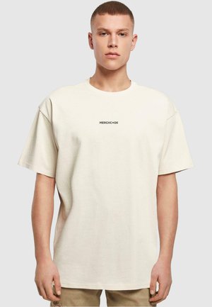 Cremefarvet oversized t-shirt lavet af bomuld, med rund halsudskæring og korte ærmer, med et lille sort "MERCHCODE" logo trykt centralt.
