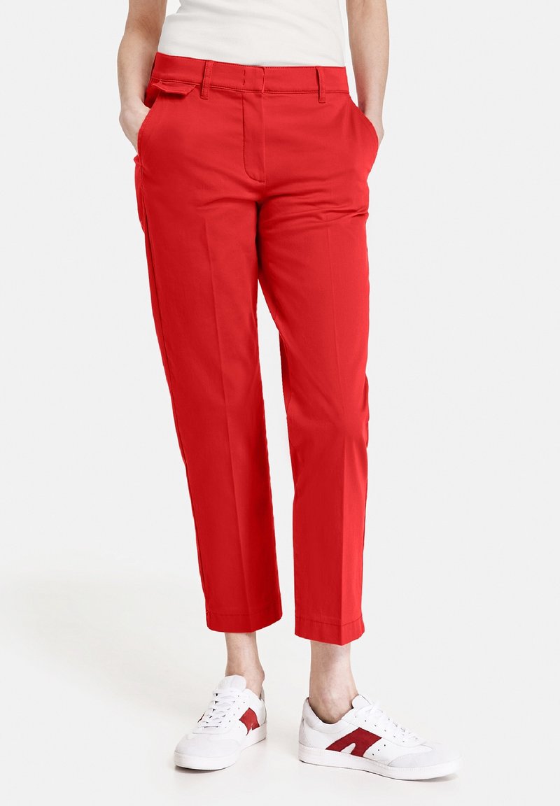 Pantalon rouge sur mesure à jambes droites avec poches latérales, assorti à des baskets blanches avec des touches rouges. Tissu à la texture lisse.