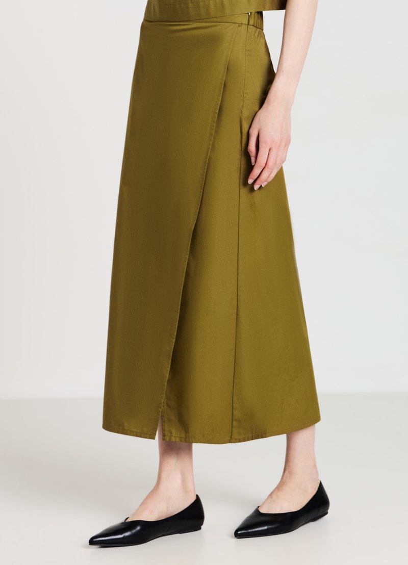 Gonna avvolgente verde oliva in un tessuto liscio, a lunghezza ginocchio, con una slitta laterale. Abbinata a scarpe flat nere a punta, che mostrano un design elegante.