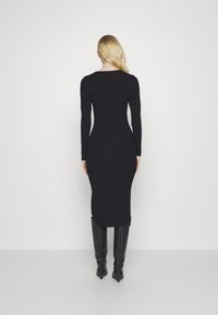 Abito a maglione nero a coste con maniche lunghe, silhouette aderente, lunghezza a metà polpaccio e spacco laterale, abbinato a stivali neri al ginocchio.