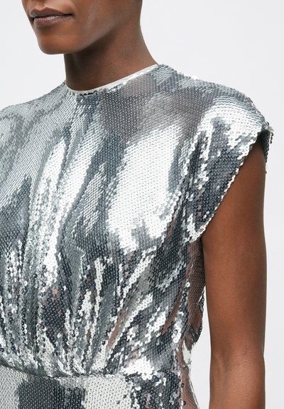 Sudraba spīduma kleita ar augstu kakla izgriezumu, īsām piedurknēm un pieguļošu siluetu, kas ir ar mirdzošu tekstūru un gludu apdari.