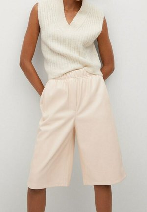 Person iført ærmeløs cremefarvet striktop og beige, løstsiddende knælange shorts med høj talje, stående med hænderne i lommerne.