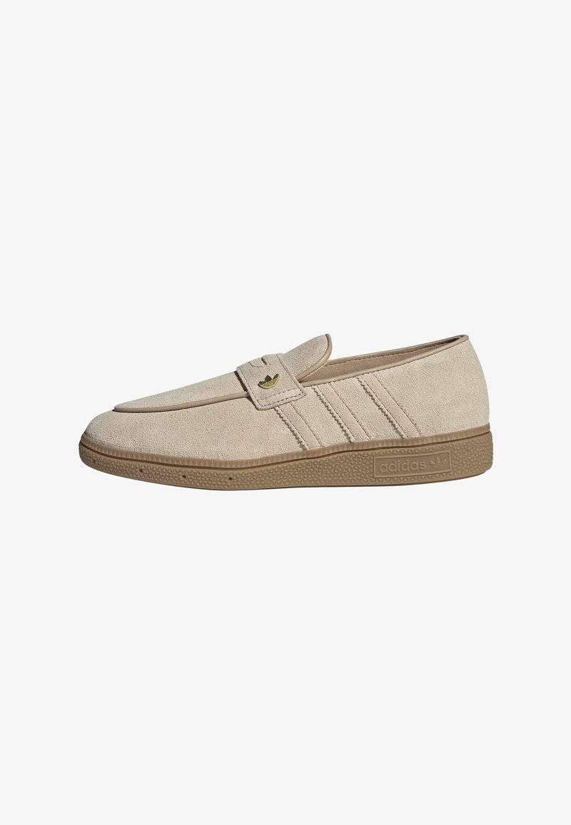 Beige mokkanahkainen slip-on-tennari ruskealla kumipohjalla, Adidas-logo sivulla ja hihnassa sekä kolme ommeltua sivuraitaa.