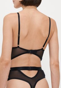 Ensemble en lingerie en maille noire avec des bretelles réglables, fermeture par crochet et design découpé. Présente une texture lisse et des accents minimalistes.