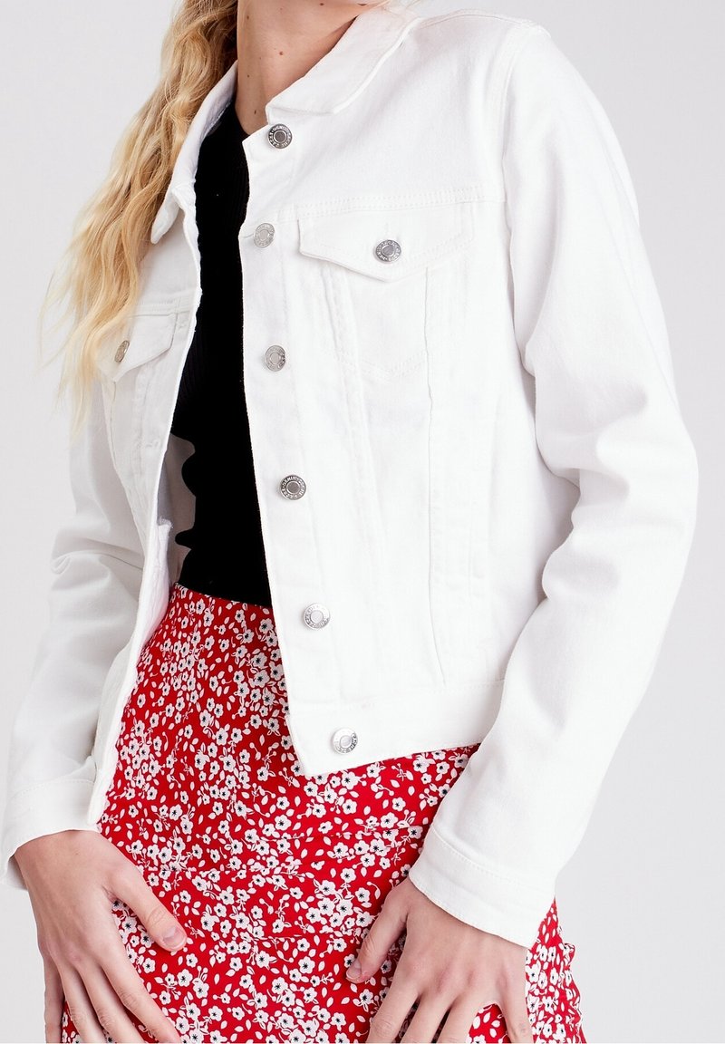 Veste en jean blanche avec boutons argentés, dotée d'un col, de deux poches poitrine et d'une coupe ajustée. Associée à une jupe rouge à motif floral.