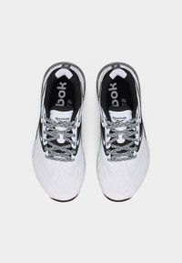 Ζευγάρι λευκά και μαύρα παπούτσια τρεξίματος Reebok με κορδόνια με σχέδιο, φαίνονται από ψηλά σε λευκό φόντο.