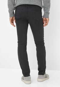 Zwarte denim jeans met een slim fit, zichtbare stiksels en twee achterzakken. De drager heeft grijze sneakers met lichte accenten.