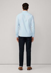 Camicia azzurro chiaro a maniche lunghe con colletto classico, abbinata a jeans denim scuri e scarpe marroni, vista di spalle.