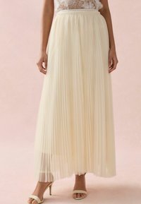 Plisowana spódnica maxi w jasnym kremie, z szerokim elastycznym paskiem w talii. Półprzezroczysty materiał układa się elegancko, tworząc zwiewną sylwetkę.
