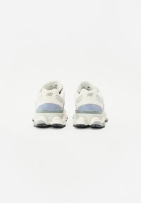 Baskets blanches et bleu clair avec une tige en tissu texturé, une semelle en caoutchouc courbée et une semelle intermédiaire transparente. Présentent le logo "NB" sur le talon.