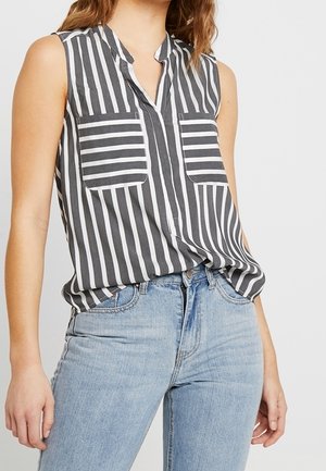 Szara i biała, bezrękawnikowa bluzka w paski z kołnierzykiem, dwoma przednimi kieszeniami i luźnym krojem, zestawiona z jasnoniebieskimi dżinsami.