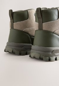 Grüne Wanderschuhe aus Leder und Wildleder, ausgestattet mit einer strukturierten Außensohle, verstärkter Ferse und einer Zuglasche für einfaches An- und Ausziehen.