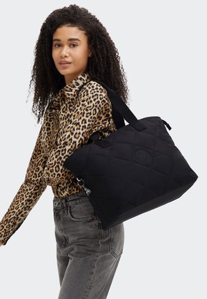 Borsa a tote nera trapuntata con due robusti manici, caratterizzata da una superficie testurizzata e un logo, portata contro una maglietta con stampa leopardata.