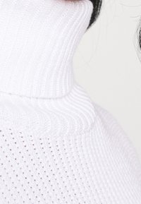 Weißer gestrickter Rollkragenpullover mit einem strukturierten Rippenmuster, ausgestattet mit einem hohen Kragen und einer engen Passform um den Hals.