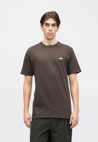 Brun bomulds t-shirt med korte ærmer og rund hals, prydet med et lille hvidt "OBEY" logo på venstre brystområde.