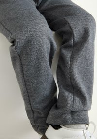 Grå bukser med fiskebensmønster lavet af struktureret stof, med tapered ben og elastiske manchetter, parret med hvide og grå sneakers.