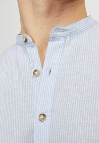 Camicia a righe blu chiaro con colletto e parte anteriore con bottoni. Presenta un colletto arrotondato e un piccolo anello al collo. Texture del tessuto liscia.