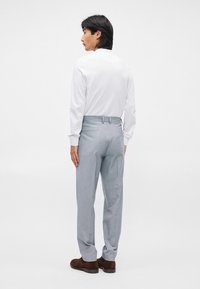 Ανοιχτό γκρι καρό παντελόνι με κομψή εφαρμογή, που διαθέτει βρόχους ζώνης, τσέπες και σχέδιο με επίπεδο μπροστινό μέρος. Φοριέται με άσπρη μακριά μπλούζα.