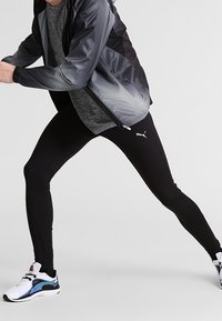 Leggings atletici neri abbinati a una maglietta grigia a trama e a una giacca nera a righe. Presentano un design elegante e il marchio Puma.