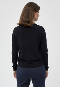 Maglione nero lavorato a maglia con maniche lunghe e scollatura rotonda, dotato di polsini e orlo a costine, indossato con pantaloni scuri, con focus sulla vista posteriore.