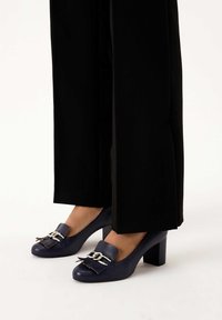 Navy leather high-heeled shoes with a rounded toe, featuring a silver-toned hardware accent and decorative fringe detail.