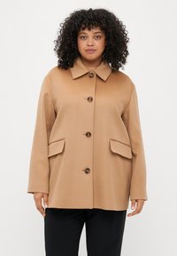 Απαλή καφέ παλτό από μείγμα μαλλιού με κολάρο, μπροστινά κουμπιά και δύο μεγάλες πλαϊνές τσέπες. Διαθέτει χαλαρή εφαρμογή και λεία υφή.