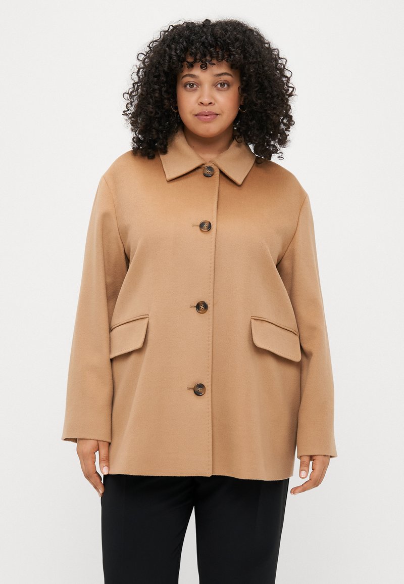 Απαλή καφέ παλτό από μείγμα μαλλιού με κολάρο, μπροστινά κουμπιά και δύο μεγάλες πλαϊνές τσέπες. Διαθέτει χαλαρή εφαρμογή και λεία υφή.