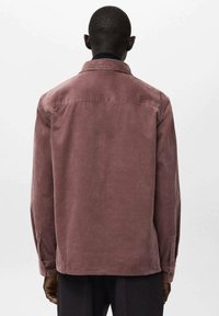 Manchesterskjorta i dammig rosafärg med krage, långa ärmar och knappmanschetter. Har vertikala ränder och en avslappnad passform.