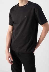 T-shirt nera a girocollo realizzata in tessuto liscio, con un piccolo logo "ck" sul petto e la scritta "Calvin Klein" sul colletto.