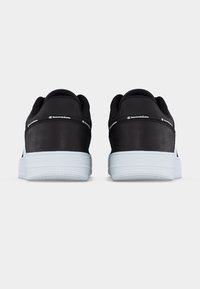 Ζεύγος μαύρων και λευκών αθλητικών παπουτσιών Champion, εμφανιζόμενα από πίσω με το κείμενο του λογότυπου στον γύρο της φτέρνας, σε λευκό φόντο.