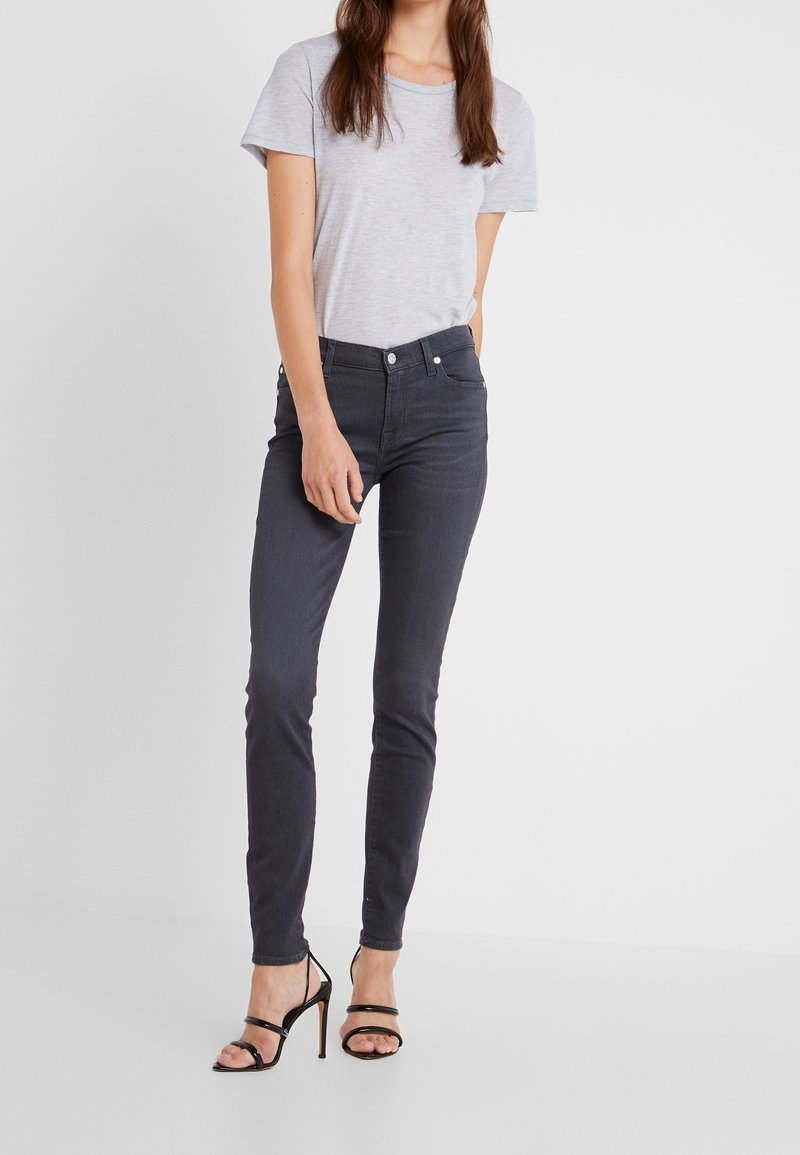 Camiseta gris de manga corta combinada con jeans negros ajustados, que presentan una cintura de altura media y un ligero estiramiento. Sandalias de tacón alto negras con tiras.