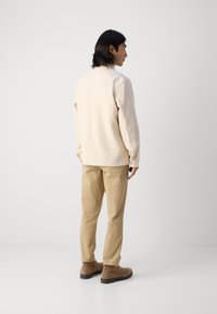 Beige long-sleeve shirt with a relaxed fit, paired with light brown trousers and brown ankle boots; smooth texture and minimal seams.