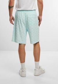 Lyse turkis shorts med et struktureret mønster, der har en elastisk talje og sidelommer, båret med hvide sneakers og sokker.