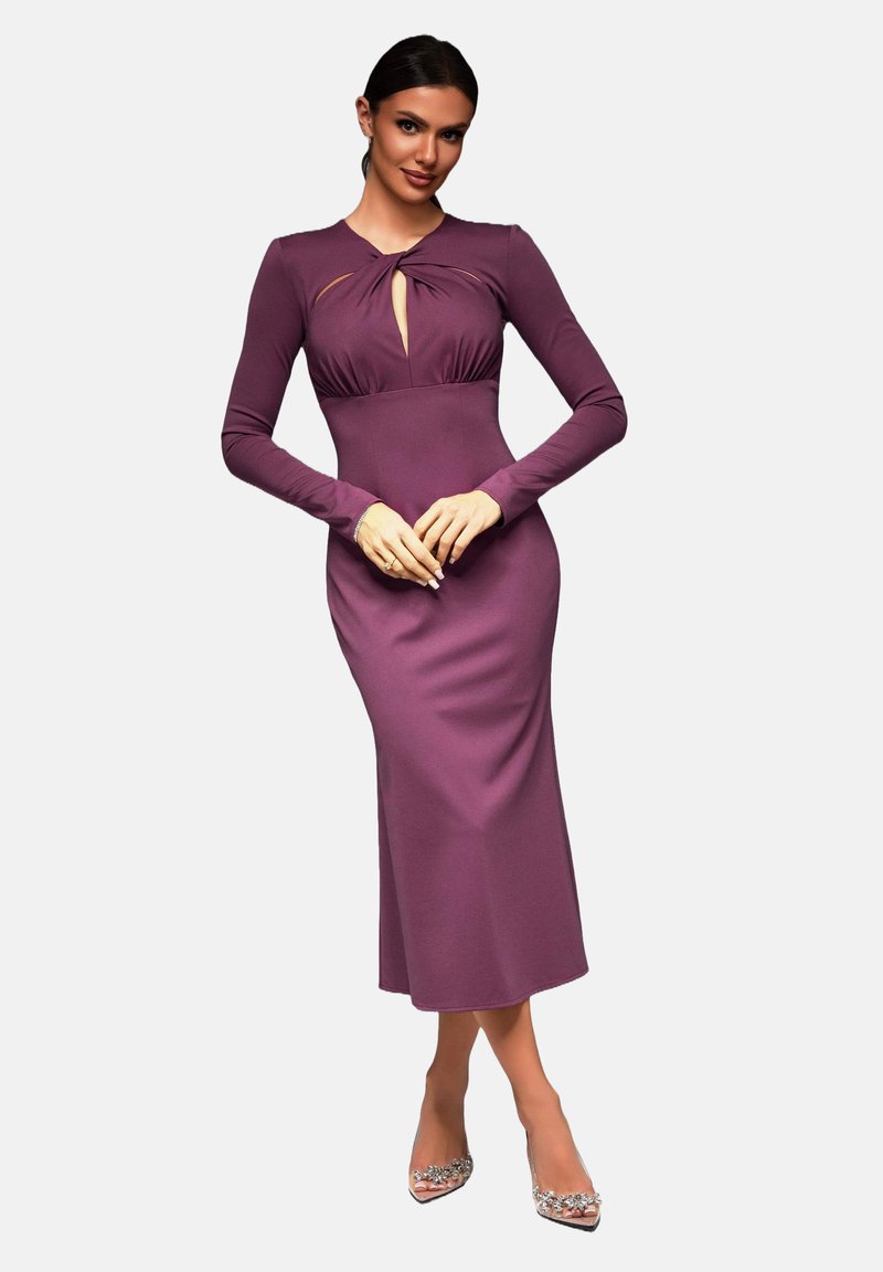 Kroppsnära lila klänning med lång ärm, nyckelhålsutskärning vid bröstet och elegant design, matchad med prydliga högklackade skor.