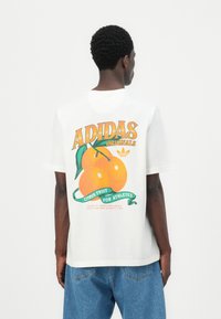 Balta medvilninė marškinė su dideliu grafikų atvaizdu, vaizduojančiu dvi apelsinus, žalia juostelė su užrašu "CITRUS FRUIT FOR ATHLETES" ir logotipų akcentais.