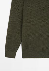 Maglione verde scuro lavorato a maglia con superficie testurizzata, maniche lunghe e polsini a coste. L'orlo è dritto e il tessuto appare morbido.