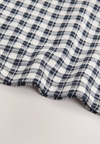 Tissu de coton avec un motif à carreaux bleu marine et blanc, présentant une surface texturée et un bord doux et ondulé.