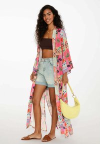 Kolorowy kimono z kwiatowymi i geometrycznymi wzorami, lekkiego materiału, z otwartym przodem, noszone na brązowym topie i dżinsowych szortach z wysokim stanem.