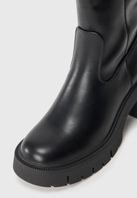 Black leather ankle boot with a glossy finish, thick rubber sole, and subtle stitching details. Features a rounded toe and side elastic panel.