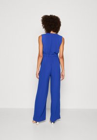 Ärmlös blå jumpsuit med insvängd midja, vida ben och en strukturerad tygkonstruktion. Har en bakknäppning och en minimalistisk design.