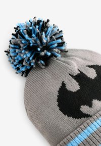Graue Strickmütze mit einem großen schwarzen Batman-Logo, versehen mit einem bunten Pompon, der aus blauem, schwarzem und grauem Garn besteht. 