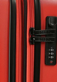 Roter Hartschalenkoffer mit strukturierten Oberflächen, zwei schwarzen Reißverschlüssen, einem schwarzen Schließmechanismus mit einem Kombinationsziffernrad und verstärkten Kanten.