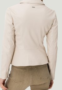Giacca in pelle crema con silhouette aderente, colletto a revers e dettagli delle cuciture sul retro, abbinata a jeans verde oliva.