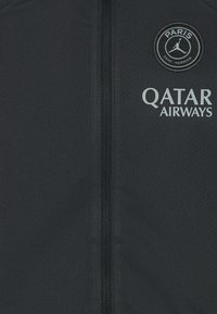 Schwarze Sportjacke mit zentralem Reißverschluss, rundem Logo mit "PARIS SAINT-GERMAIN" und "QATAR AIRWAYS" in Hellgrau gedruckt.