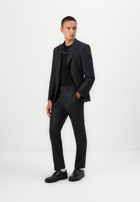 Schwarzer Anzug mit einem maßgeschneiderten Blazer und schmal geschnittenen Hosen, kombiniert mit einem schwarzen T-Shirt und schwarzen Lederschuhen. Glatter Stoff, minimalistisches Design.