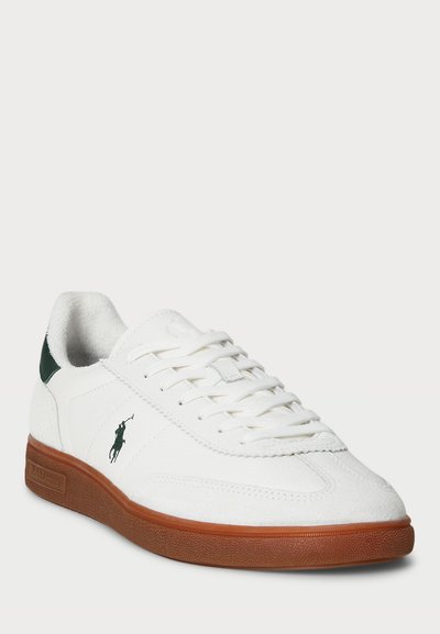 Baltas sneakers ar strukturētu virsmu, zaļiem akcentiem uz papēža un brūnu gumijas zoli. Satur plakanās šņores un logotipu uz sāna.