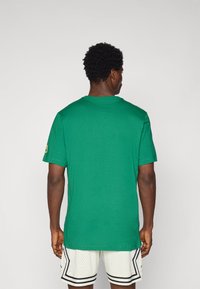 Camiseta de algodón verde con cuello redondo y mangas cortas. Cuenta con un logo en la manga izquierda y combina con pantalones cortos de malla ligeros.