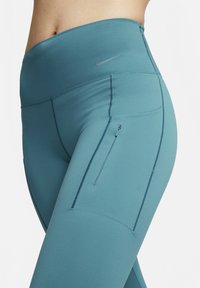 Turkusowe legginsy z wysokim stanem, z boczną kieszenią na zamek błyskawiczny oraz płaskimi szwami dla wygody. Na wykończeniu pasa widoczne jest logo Nike.